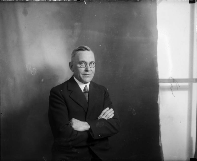 Studio portrait of Mayor Ben Stapleton, Denver, Colorado; he wears wire rim glasses and a suit.
