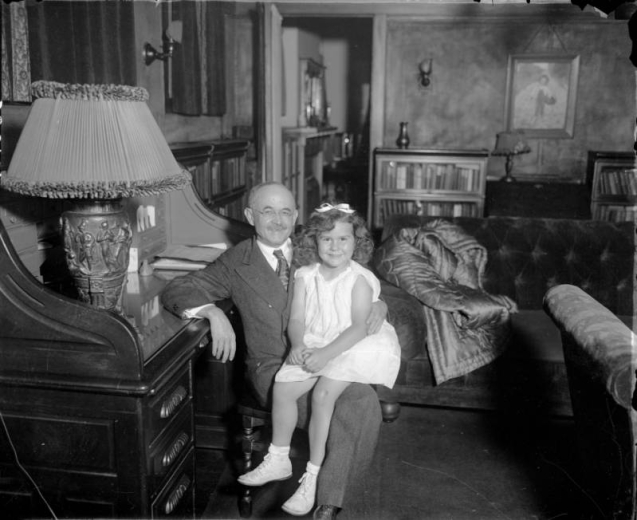 Portrait of Judge Benjamin Barr Lindsey, with a girl on his lap. He sits at a desk, by a Greek bas-relief lamp.