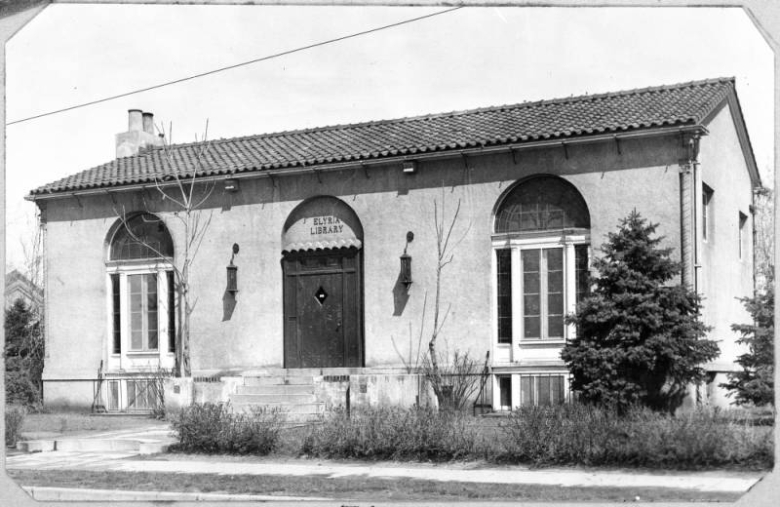 An exterior view of the Elyria branch library located on 47th Avenue and High Street in Denver, Colorado. The spanish style building was designed by architect H. J. Manning; it features red tiled roof, arched windows and doorway. The Elyria branch was closed in 1952.