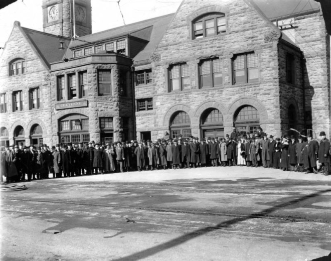 Men pose outdoors at the Union Pacific Railroad Depot in Cheyenne, Wyoming. The stone masonry building has a clock tower and arched windows.