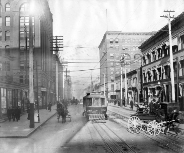 View of Denver Tramway Company trolley Park Hill number 230 on 17th (Seventeenth) Street in Denver, Colorado. Downtown business signs and awnings read: "Postal Telegraph Commercial Cables", "Mutual Life", "National Life U.S.A.", "Brunskill Sign Painting", "Jackson and Co. Employment Office", and "Boston Lunch". On the street and sidewalks are pedestrians, horses, buggies, wagons, and barber shop poles.