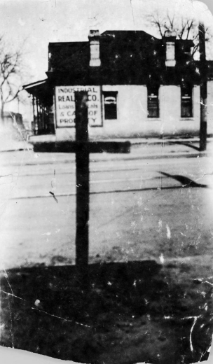 View of a cross burned in Clarence F. Holmes' yard by the KKK near his office at 2602 Welton Street in the Five Points neighborhood of Denver, Colorado. A sign on a nearby building reads: "Industrial Real[ty] Co. [...]"