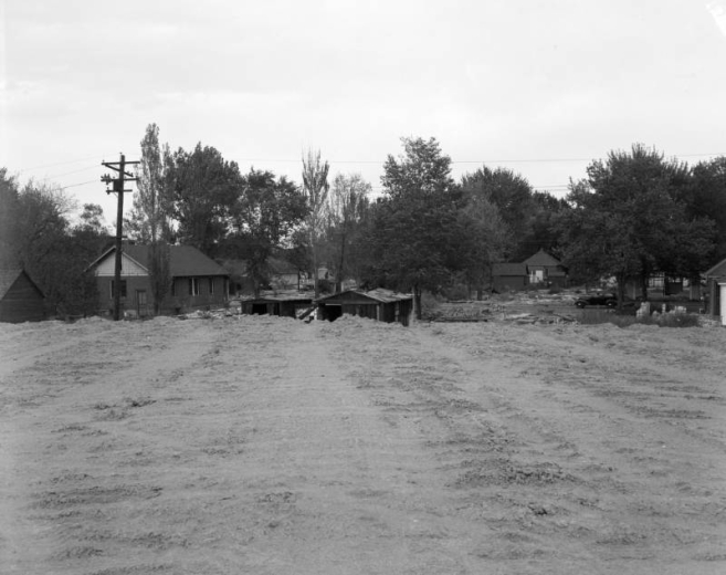 View of the preparation for Valley Highway (I-25) construction, in Denver, Colorado; shows graded earth, houses, and a car.