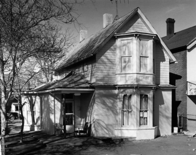 View of 2523 Stout Street in the Curtis Park neighborhood (Five Points) in Denver, Colorado; shows a house with bay windows, paint masked second story windows, and a porch with chairs.