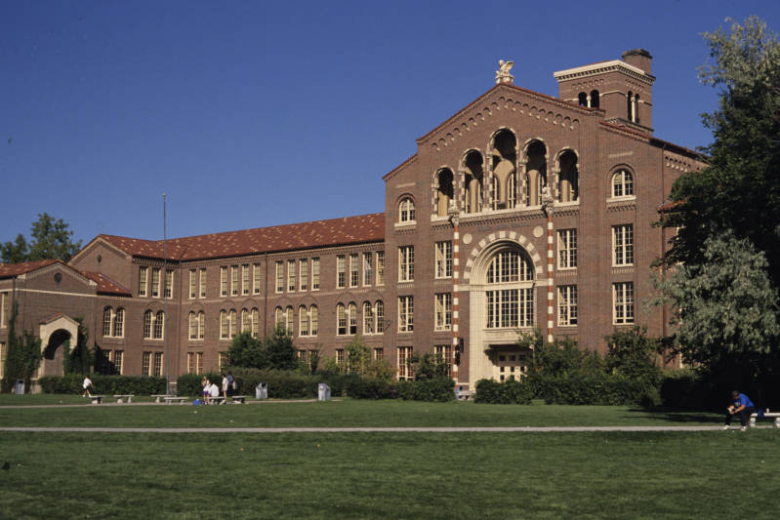 View of South High School (1924; William E. and Arthur A. Fisher, architects) at 1700 East Louisiana Avenue in the Washington Park neighborhood of Denver, Colorado. Shows a four-story, red brick, Italian Renaissance Revival-style school building with terracotta trim, a red tile roof, and a clock tower. The main entrance doors are set on the ground floor of a three-story round arch. Above the entrance is a loggia with five arches. A griffin tops the roof.