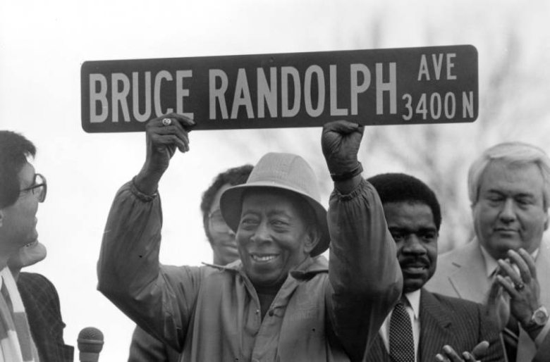 "Daddy" Bruce Randolph, an African-American restaurant owner and philanthropist, holds a street sign that bears his name during a ceremony in Denver's Five Points neighborhood, Colorado. Mayor Federico Pena, City Councilman Hiawatha Davis, and other men stand nearby.