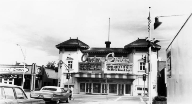 View of the Ogden Theater on Colfax Avenue in Denver, Colorado. The two-story building has a tile roof and a marquee that reads: "James Garner Debbie Reynolds 'How Sweet It Is' 'No Way To Treat A Lady.'"