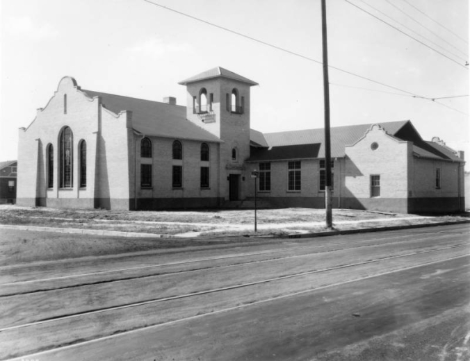 View of a church at Sixth Avenue and Adams Street in the Congress Park neighborhood of Denver, Colorado; features include mission style pediments and a square tower. Streetcar tracks are in the foreground.