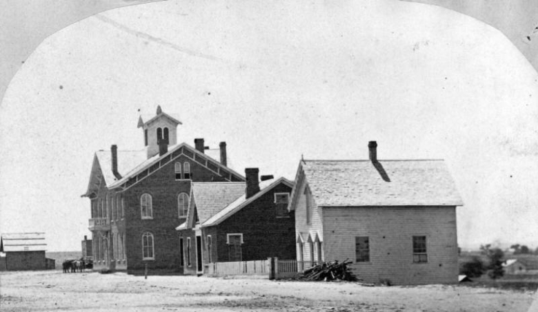 View of the Colorado Seminary, the Governor John Evans house, and an unidentified house on 14th (Fourteenth) and Arapahoe Streets in downtown Denver, Colorado. The brick buildings have hip roofs, chimneys, and a cupola.