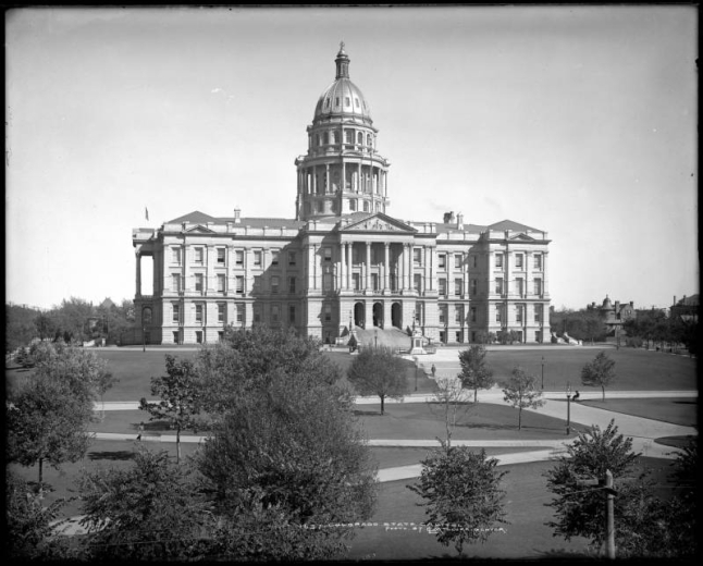 Exterior view of Colorado State Capitol and grounds, Denver, Colorado; Capitol dome with gold-leaf completed in 1908; landscaped grounds, trees, sidewalks; large residence across street from Capitol, center right.