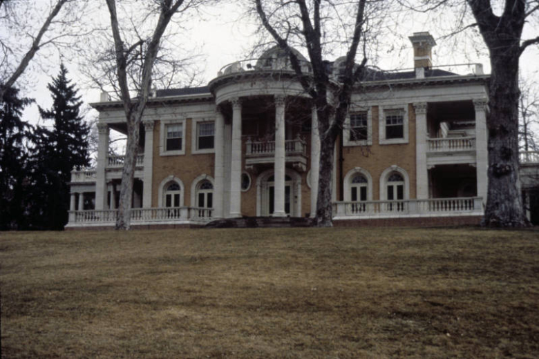 View of the west elevation of the Grant-Humphreys Mansion (1902: Theodore Davis Boal and Frederick L. Harnois, architects) in the Capitol Hill Neighborhood (East Seventh Avenue Historic District), Denver, Colorado. The Neoclassical style building has a semicircular portico on the west elevation supported by fluted Corinthian Columns. Shows Georgian balustrades on the first and second story balconies as well as the heavily damaged rooftop balustrade.