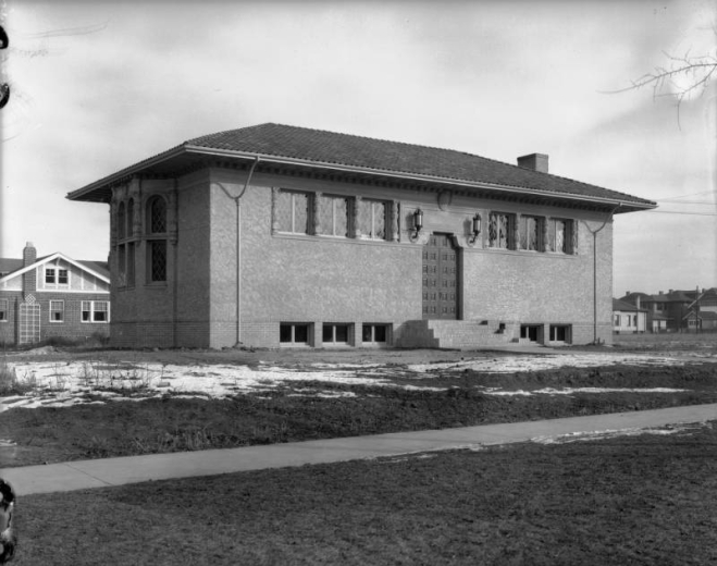 View of the Park Hill Branch of the Denver Public Library at Dexter Street and Montview Boulevard in Denver, Colorado; features a tile roof, stucco finish, leaded glass, and a bay window with entablature.
