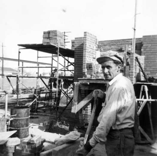 View of construction of the Ross-Barnum Branch of the Denver Public Library in Denver, Colorado; a man holds a shovel. Bricks are on a scaffold.