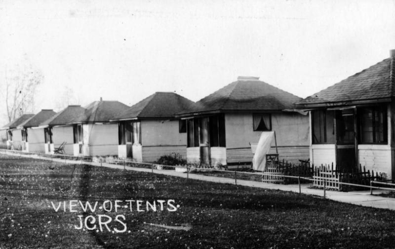 Exterior view of a row of quarantine tents at the Jewish Consumptive Relief Society (J.C.R.S.) sanatorium, 1600 Pierce Street, Denver, Colorado. The tent houses are small, square structures with wood frames.