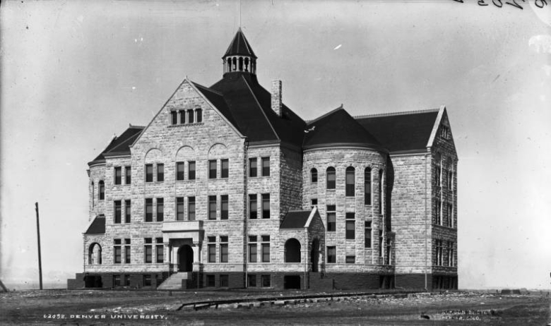 View of University Hall (Old Main) at Denver University in Denver, Colorado. The rusticated stone building has a tower with conical roof, cupola, and hip roof.