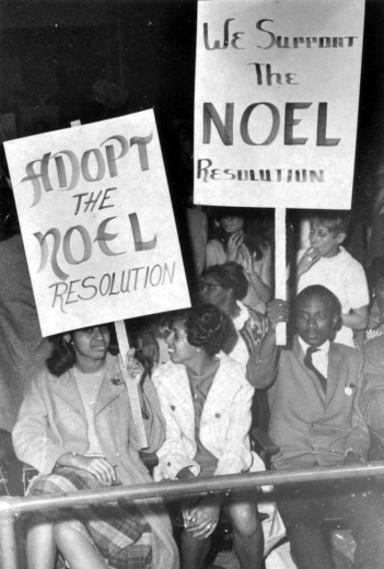 Black (African American) men and women hold picket signs in Denver, Colorado during a political demonstration. Picket signs read: "We Support the Noel Resolution."