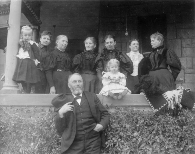 A group portrait of William N. Byers and his wife, Elizabeth; shows his sisters, an unidentified female relative, and possibly grandchildren; they pose on the porch of his residence at 171 South Washington Street (Speer neighborhood), Denver, Colorado.
