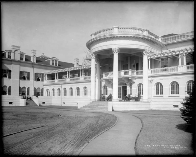 Exterior view of Oakes Home, 2825 West 32nd (Thirty-second) and Decatur, Denver, Colorado; built by Reverend Frederick W. Oakes in 1895; dirt driveway leading to Grace House (rotunda with columns) with men seated on lounge or rocking chairs; wheelchair on side porch, open windows. The first organized institution to care for tubercular victims in Denver & second in United States. All buildings except chapel torn down in early 1980's.