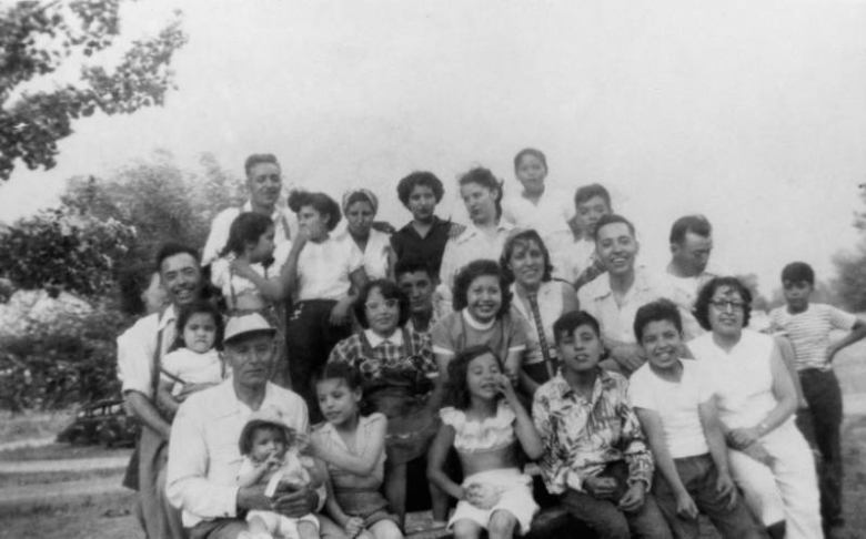 Members of the Gallegos and Torres families, residents of the Auraria neighborhood, pose in an unidentified park in Denver, Colorado. Infants, boys, girls, men, and women are in the group of unidentified family members.