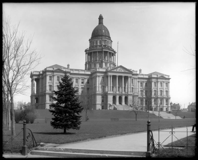 Exterior view of Colorado's State Capitol building located in Denver; completed in 1895; photograph taken from Broadway and Colfax approximately ten years later; includes wrought iron fence and park benches.