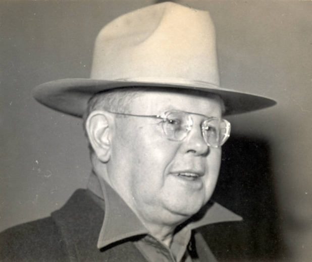 Colorado Governor Ralph L. Carr smiles, he wears eyeglasses and a felt hat.