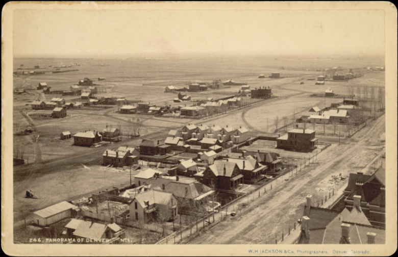 Aerial view of houses on probably Grant Street near 17th (Seventeenth) Street in the North Capitol Hill neighborhood of Denver, Colorado. Shows dirt roads and Victorian houses with gabled or hipped roofs and chimneys. Wagon roads curve through open lots.