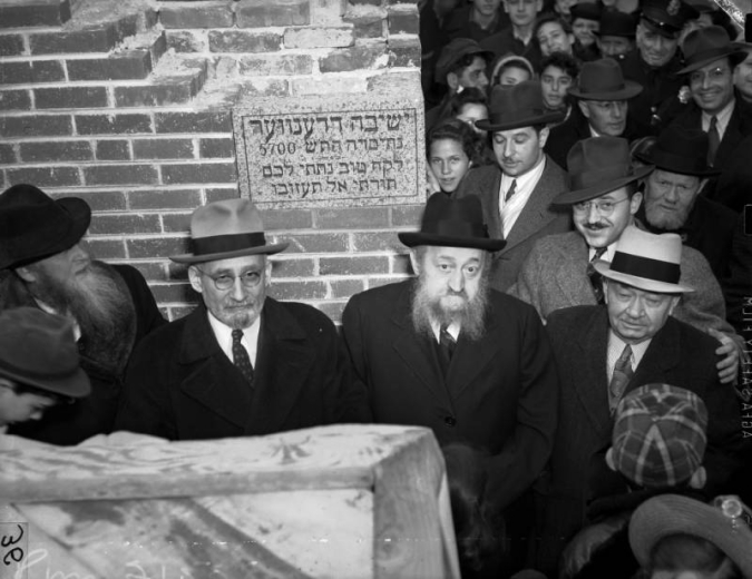 Men pose by the cornerstone at Yeshiva Toras Chaim at 1400 Quitman Street in the West Colfax neighborhood of  Denver, Colorado; men, women, and a police officer are in the background. Rabbi Mordechai Burstein, Ed Rosenbloom, Ed Grinus, Judah Gordon, and S. J. Rosenbloom are in the foreground.