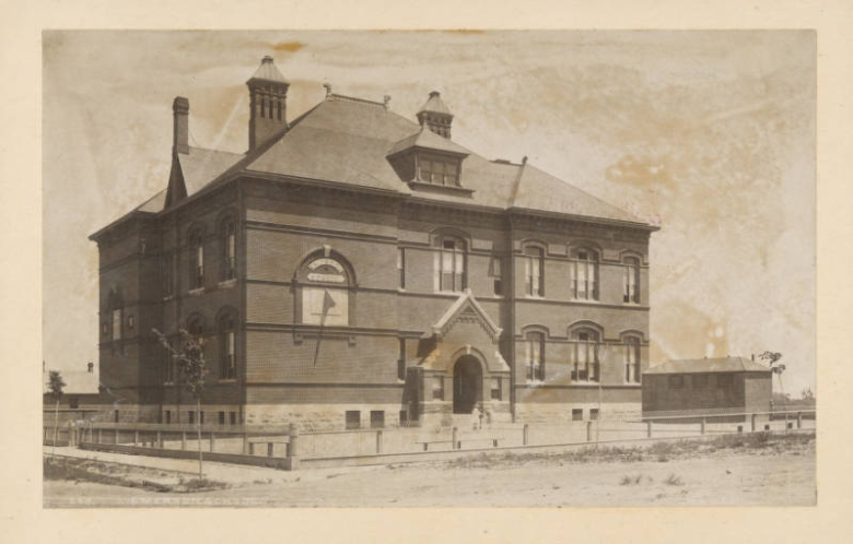 A view of Emerson School, designed by Robert S. Roeschlaub, at the corner of 14th (Fourteenth) and Emerson streets in the Capitol Hill neighborhood of Denver, Colorado. The school is constructed of brick and has a sundial mounted on the side of the building. A sign on the building reads "Emerson School".