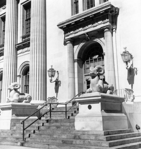 View of the facade at an entrance to the Neo-Classical style Byron White U.S. Courthouse at 1823 Stout Street in Denver, Colorado. Shows an arched entrance, fluted columns, lanterns and two sculptures of Rocky Mountain Sheep by Gladys Caldwell Fisher. The statues are mounted on pedestals and flank a stone staircase.