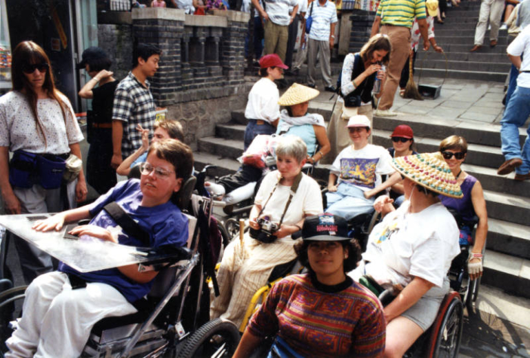 Laura Hershey and others protesting lack of access to United Nations Fourth World Conference on Women in Beijing, China in August 1995. Photograph was taken in Huairo, China and pictures the first large-scale protest regarding accessibility to the conference. To Laura's right is friend Laurie Gery. Photographer unknown.