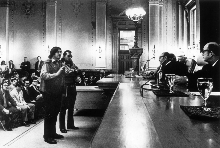 Two Native American men, members of the American Indian Movement (AIM), stand before the Justices of the Colorado State Supreme Court to argue against perceived discrimination toward Native Americans with regard to bar examinations in Denver, Colorado. Onlookers fill the gallery.