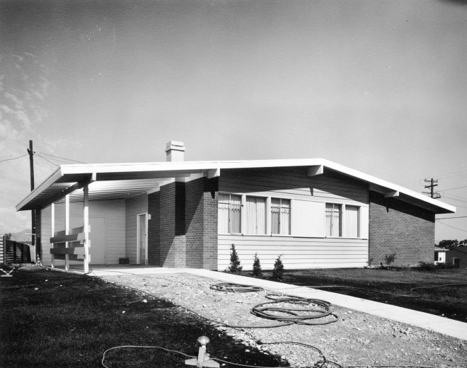 View of a brick and frame house in the Harvey Park Addition of Denver, Colorado; the California bungalow style residence has a carport. The house was built by Carey Construction and advertised as a "Holiday Home."