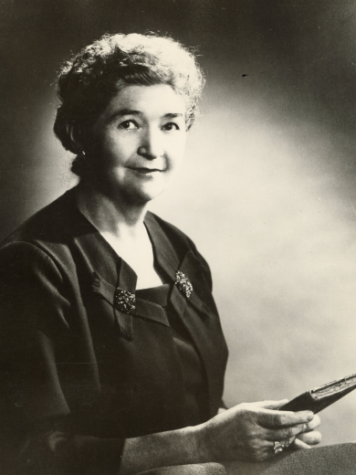 Portrait of Agnes Wright Spring, posing in a black blouse and holding a book.