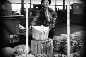 A man stands in front of a truck with a basket of produce