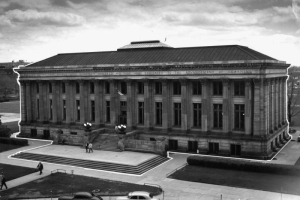 North facade of the Denver Public Library, Civic Center, Denver, Colorado. The Greek revival style Carnegie building features gray Turkey Creek Sandstone construction, fourteen fluted columns with Corinthian capitals, hipped roof and skylight. Inscription along freize reads: "Erected in the year of our Lord nineteen and nine and dedicated to the advancement of learning." Automobiles park along Colorado U. S. 40 or Colfax Avenue.