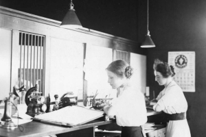 Two women work at ledgers while standing at a desk in a bank in Paonia, Colorado in Delta County.