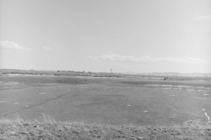View of Rocky Flats in Golden, Jefferson County, Colorado (a Department of Energy site that manufactures plutonium triggers for nuclear weapons); shows buildings, fields, a water tower, and mountains.