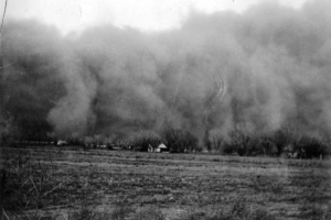 View of a huge dark cloud of dust possibly in Walsh, Baca County,  or Holly, Prowers County, southeastern Colorado. A house and line of trees  is barely visible. The devasting dust bowl carried top soil for miles.