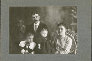 Studio portrait of Pablo C. de Baca, his wife Emilia Rudolph C. de Baca, their unidentified son and an unidentified infant. Pablo wears a dark suit and tie, has his hair parted in the middle and has a waxed mustache. His wife Emilia wears a blouse with puffed sleeves. The young boy wears a dark vest and a shirt with a lace Bertha collar and an over sized bow tie. The baby wears a dark dress and has its hair parted in the middle.