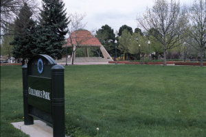 View of the sign for Columbus Park between West 38th (Thirty-eighth) and West 39th (Thirty-ninth) Avenues and Navajo and Osage Streets in the Sunnyside Neighborhood, Denver, Colorado. The sign reads: "Denver Department of Parks and Recreation Columbus Park." A picnic shelter, an Aztec inspired pavilion with a red stepped pyramid shaped roof and stucco supports, is in the distance.