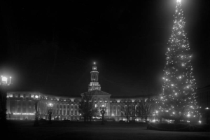 Shows an illuminated night view of the City and County Building decorated for Christmas at Civic Center park on Bannock street in Denver, Colorado. A tree in front of the building is decorated with lights and ornaments.