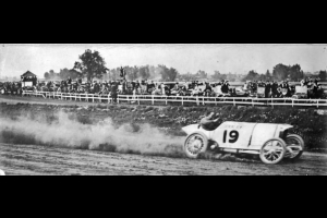 View of a dirt track auto race with car #19, probably at Overland Park in Denver, Colorado. Spectators watch from behind the fence.