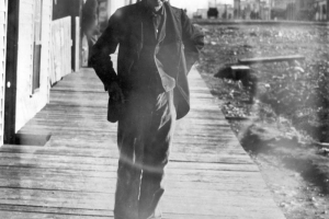 A Chinese man poses on a wooden sidewalk near a business district possibly in Colorado. A nearby sign on a building reads: "[?]ng Lee [La]undry".