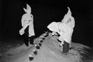 Ku Klux Klan memeber light candles in metal cans buried in a dirt mound probably in Denver, Colorado. They wear hoods and robes.