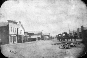 Very early photograph showing Denver, Colorado, then called Denver City. Covered wagons are parked on Larimer Street. Two-story wood frame buildings line the street.