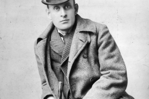 Studio portrait of Eugene Field in San Francisco, California. He holds a cane and wears an overcoat and bowler hat.