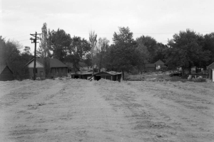 View of the preparation for Valley Highway (I-25) construction, in Denver, Colorado; shows graded earth, houses, and a car.