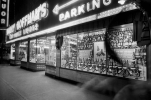 Night view of Harry Hoffman's Cut Price Liquor store at Curtis and 18th (Eighteenth) Streets in Denver, Colorado. Windows display bottles of Calvert whiskey; neon signs read "Harry Hoffman's," "Liquor," and "Free Parking."
