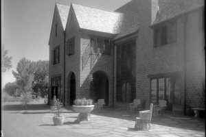 View of Mrs. George W. (Ethel R.) Gano's residence, South University Road, Denver, Colorado, a brick house with arches, picture windows, a flagstone patio, wicker furniture, and potted trees.