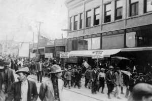 Boys march in support of UMW coal miners on strike against CF&I in Trinidad, Las Animas County, Colorado, carrying signs: "We Represent the CF&I Prosperity Slaves," "Let The Public take Over The Mines,"  "Colorado Civilization Turn Us Out in the Rain," and "Has the Governor any Respect for the State?" Men crowd sidewalks by brick businesses.